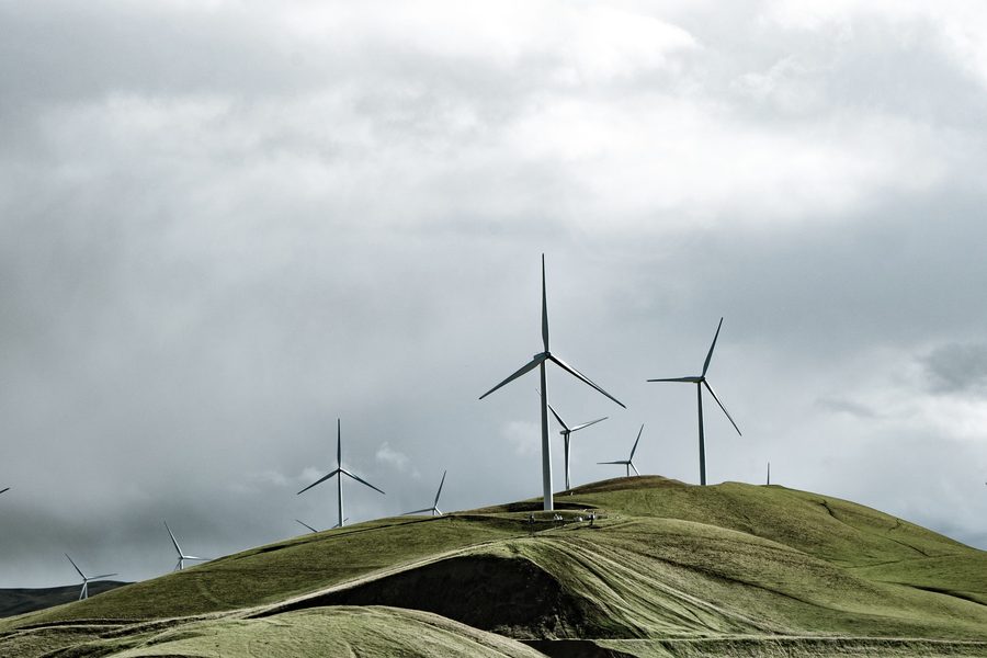 Aerogeneradores sobre una loma verde bajo nubes densas