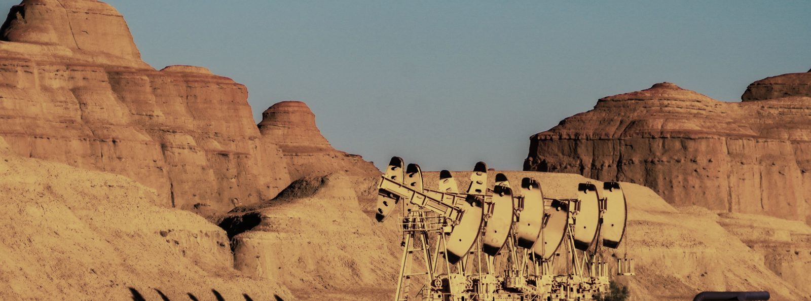 Una fila de pumpjacks trabajando bajo acantilados erosionados
